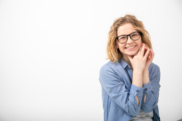 Portrait of young joyous attractive woman sit looking at camera, folding hands near face on white background. Emotions.