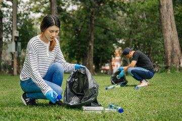 Fototapeta premium Two people keeping garbage plastic bottle into black bag at park.Clearing, pollution, ecology and plastic concept. in morning