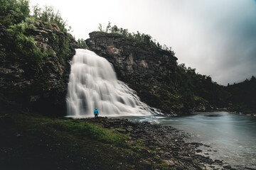 Obraz premium Scenic view of a waterfall flowing down the rocks covered with moss and plants