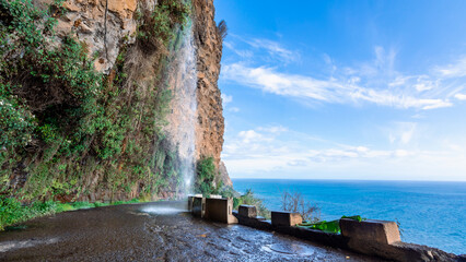 The famous Cascata dos Anjos waterfall falls on the road and cars on the coast of Madeira in Portugal