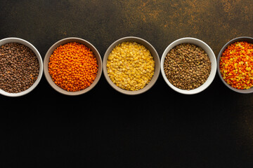 Multicolored lentils in bowls on a brown background, yellow and brown, green and orange lentils, healthy legumes, top view, copy space