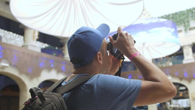 Enthusiastic tourist photographer in a blue shirt and cap taking pictures at a vacation destination