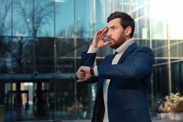 Businessman checking time on watch near building. Being late concept