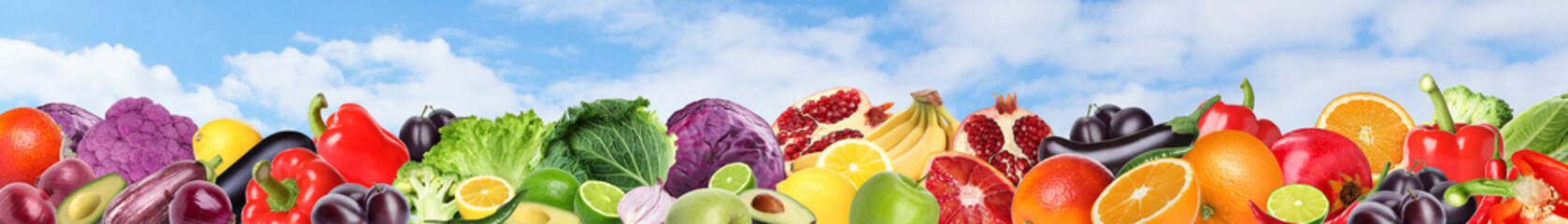 Many different fresh fruits and vegetables against blue sky with clouds. Banner design