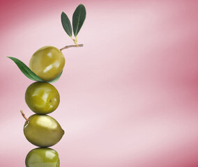 Stack of whole green olives with leaves on pink gradient background, space for text