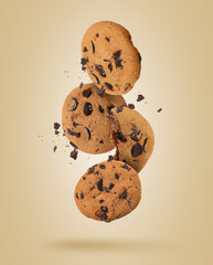 Tasty chocolate chip cookies falling on pale light brown background