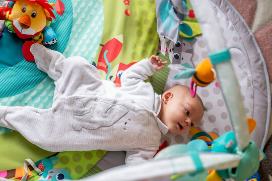 newborn baby lying on her back in a playground, baby gym to stimulate her with figures, toys and colors. concept of early stimulation of the baby