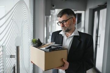 Fototapeta premium Portrait of sad dismissed senior old business man worker taking his office supplies in the box. Pensioner mature retire from work carry staff back home. Lifestyle business retirement, quit job concept