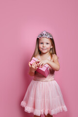 Cute sweet little princess toothy smile wearing pink dress opening present on pink background