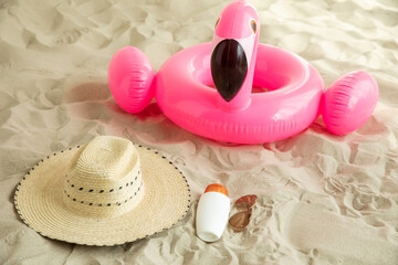 Summer travel beach flat lay composition, copy space. Straw hat, sunglasses, sunscreen lotion, sunblock cream on beach sand background. Summer vacations and spf uv-protecting skin care concept.