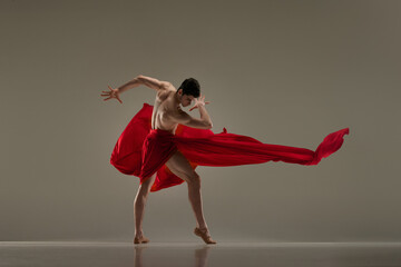 Toreador. Artistic performance with young handsome man dancing with red fabric against grey studio background. Concept of art, classical dance, inspiration, creativity, fashion, beauty, choreography
