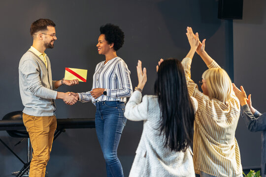 Businesswoman receiving award from businessman in front of business professionals, applauding at business seminar in office building