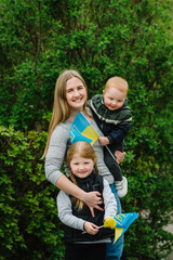 Fototapeta premium Ukrainians against war. Happy mother hugs children son and daughter. Ukrainian flag blue and yellow in hands of girl and boy. Independence Day. Constitution day. Family, unity, support. No war. Winner