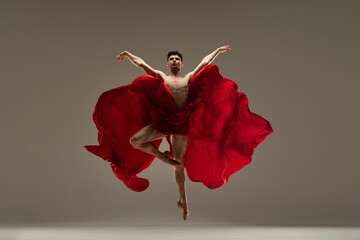 Strength. Young, muscular, handsome man, ballet dancer performing with red silk fabric against grey studio background. Concept of art, classical dance, inspiration, creativity, beauty, choreography