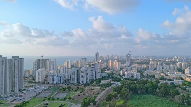 Netanya, Israel, September 3, 2022. Aerial view of the height of the city of Netanya at sunset. The sun illuminates the houses with golden rays. Blue sky with white clouds. High-quality 4k footage