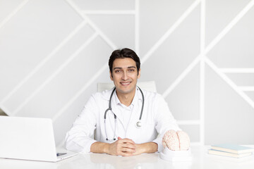 Young doctor sitting in his modern medical office and pointing on human brain model. Dementia, Alzheimer and world mental health concept