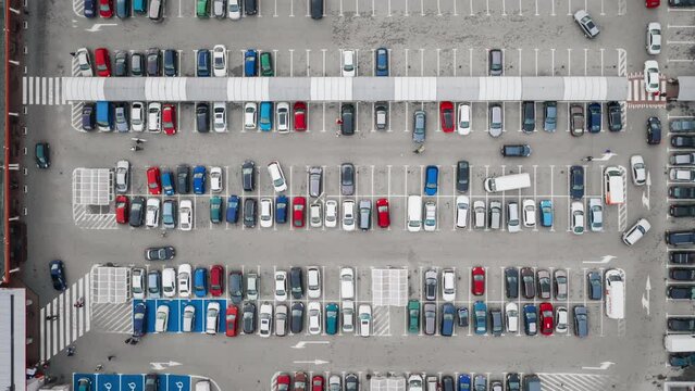 Aerial time-lapse parking near big shopping mall in city, car traffic, parking overhead drone top down view, daylight, timelapse of moving cars, busy supermarket car park