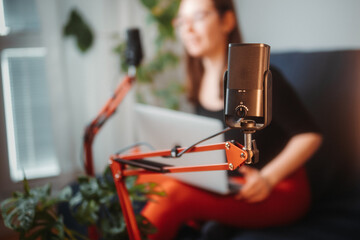 Woman recording a podcast at home studio, speaking to microphone on arm. She reads the questions loud from a computer