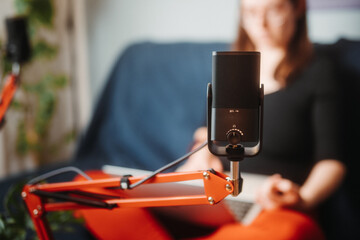 Woman recording a podcast at home studio, speaking to microphone on arm. She reads the questions loud from a computer