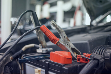 Close-up of a charging car battery with electricity using connecting cables, battery inspection. Selective focus. Blurred background.