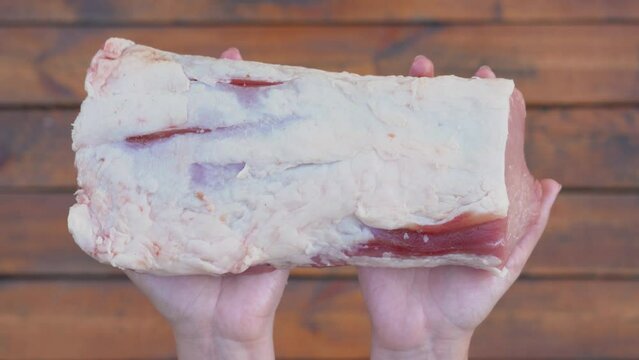 Closeup first person top view 4k stock video footage of big piece of fresh uncooked pork meat isolated on wooden board background. Woman holds piece of meat ready to cook 
