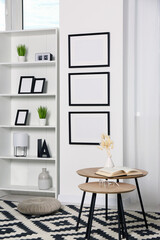 Stylish room interior with empty frames hanging on white wall near shelving unit