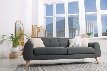 Stylish living room interior with comfortable grey sofa and clothing rack