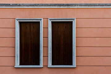 White windows covered with wooden boards of a pink building