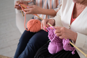 two senior women use their knitting skills to create warm, pink scarves and hats for breast cancer patients, symbolizing hope, love, and support for those battling the disease.