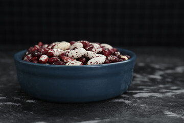 Bowl with dry kidney beans on black textured table, closeup