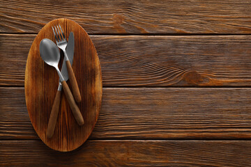 Plakat New board and cutlery on wooden table, top view with space for text