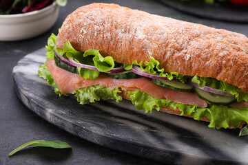 Delicious sandwich with fresh vegetables and salmon on black table, closeup