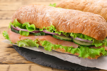 Delicious sandwich with fresh vegetables and salmon on wooden table, closeup
