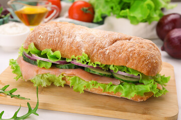 Delicious sandwich with fresh vegetables and salmon on wooden board, closeup