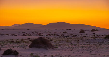 View of the dunes of Corralejo and silhouetted hills at sunset on the Canary Island of Fuerteventura, Spain.