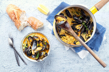 Traditional mussel bouillabaisse in white wine sauce with blue mussels and served with baguette as top view in a bowl and frying pan