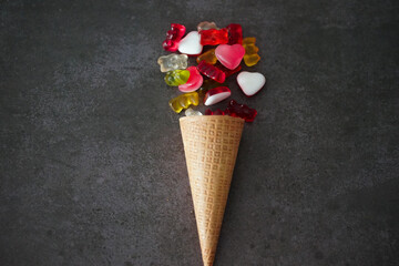 Colorful gummy bears and the hearts by the waffle cone on a black surface