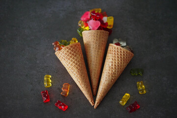 Colorful gummy bears and the hearts by the waffle cones on a black surface