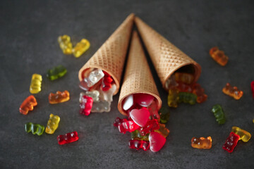 Colorful gummy bears and the hearts by the waffle cones on a black surface