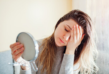 Stressed woman is sad about dirty oily and greasy hair looking in mirror at home. Healthcare....