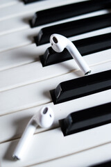 Vertical closeup of wireless earphones on black and white piano keys