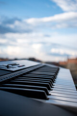 Vertical closeup of piano keys outdoors under a cloudy blue sky