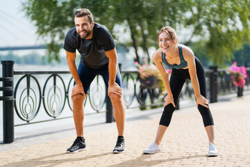 Morning jogging. Image of happy excited smiling young couple, tired runners, woman train with man, or bearded fit coach exercising outdoors. Fitness, sport city marathon workout concept.