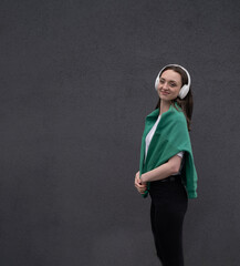 Carefree attractive brunette girl, dressed in a gray sweater, listening to music on headphones, standing on a gray background