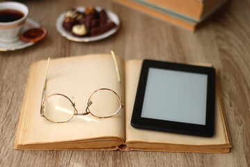 Books, reading glasses, e-reader, plate of chocolate pralines, bowl of cookies, cups of tea and lit...