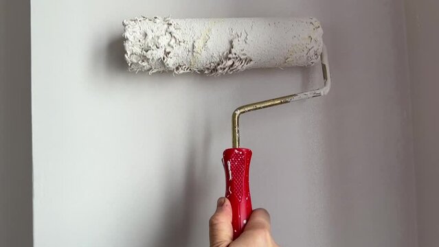 Painter man painting a blank wall, with paint stick roller. Man painting the wall with white paint with a hand roller