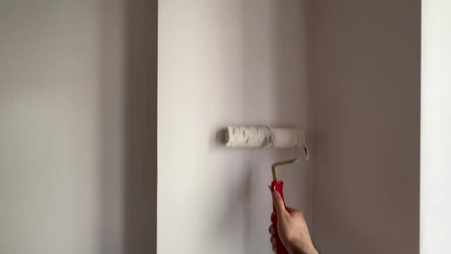 Painter man painting a blank wall, with paint stick roller. Man painting the wall with white paint with a hand roller