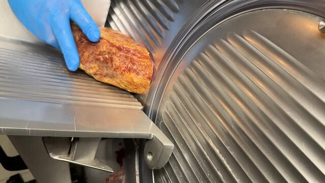 Turkish pastrami cut into thin slices. Chopping Turkish bacon on an electric food slicer. Slicing bacon with machine.