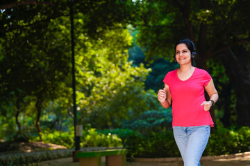 young indian woman with earphones listening music during jogging at park.
