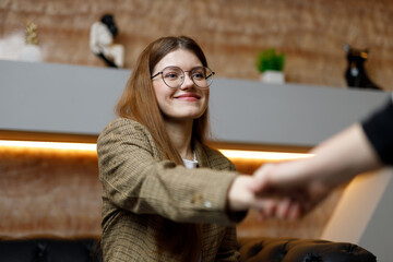 Fototapeta na wymiar Handshake with a smile by a young woman in the office, job interview.